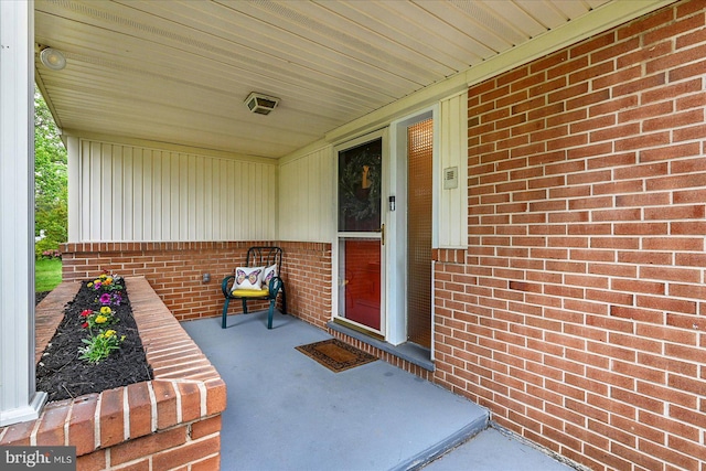 entrance to property with board and batten siding, a porch, and brick siding