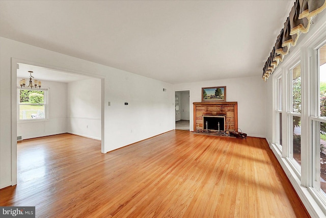 unfurnished living room featuring baseboards, a stone fireplace, a notable chandelier, and light wood-style flooring