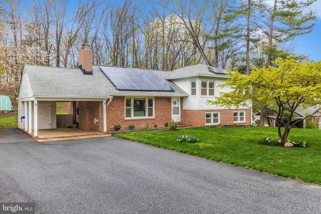 tri-level home with a front lawn, driveway, brick siding, roof with shingles, and solar panels