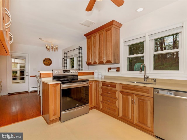 kitchen featuring a baseboard heating unit, appliances with stainless steel finishes, light countertops, a sink, and a peninsula