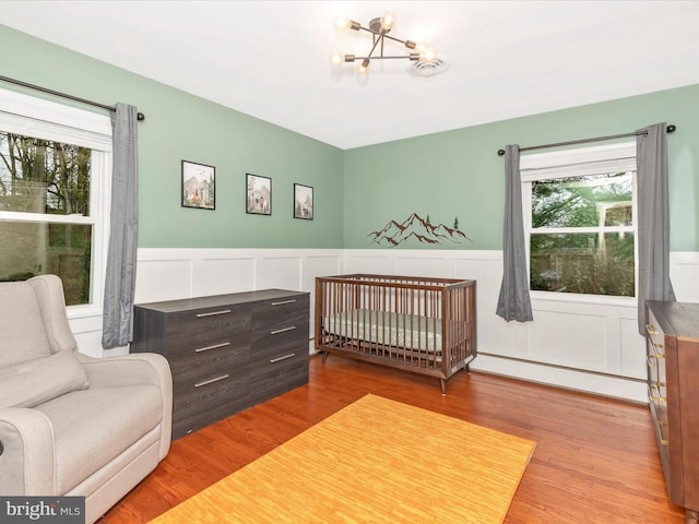 bedroom with wainscoting, wood finished floors, a notable chandelier, and a baseboard radiator