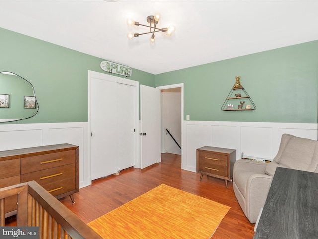 bedroom with a chandelier, a closet, a decorative wall, wainscoting, and wood finished floors