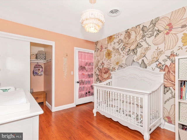 bedroom with a notable chandelier, visible vents, a nursery area, baseboards, and wood finished floors