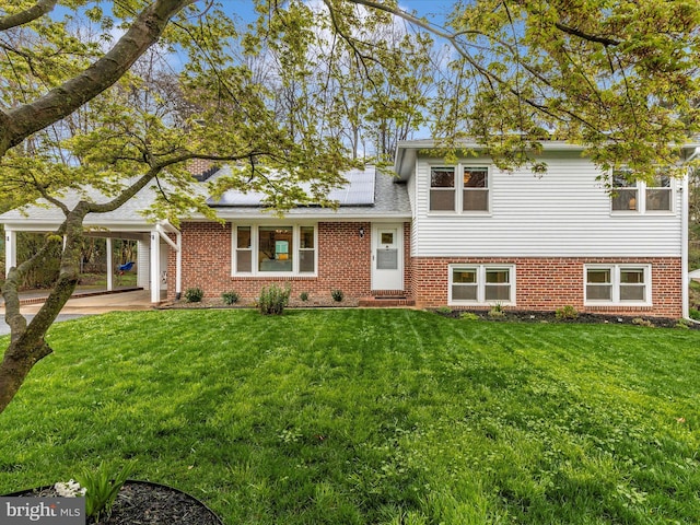 tri-level home featuring roof mounted solar panels, a carport, a front yard, and brick siding