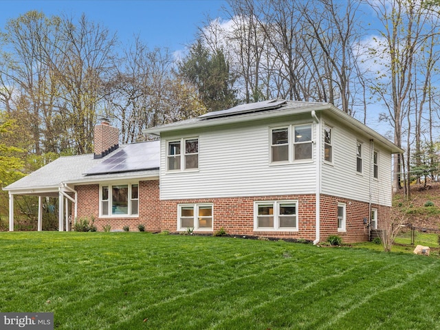 tri-level home with a chimney, brick siding, a front lawn, and roof mounted solar panels