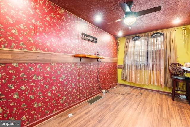 unfurnished room with a ceiling fan, visible vents, wood finished floors, and wallpapered walls