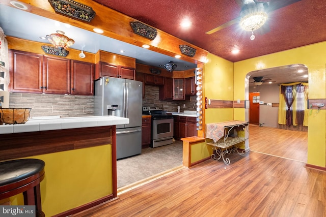 kitchen featuring stainless steel appliances, light wood-style floors, ceiling fan, and tasteful backsplash