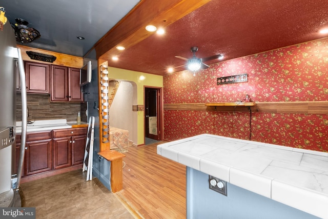 kitchen featuring arched walkways, wallpapered walls, a ceiling fan, and tile countertops