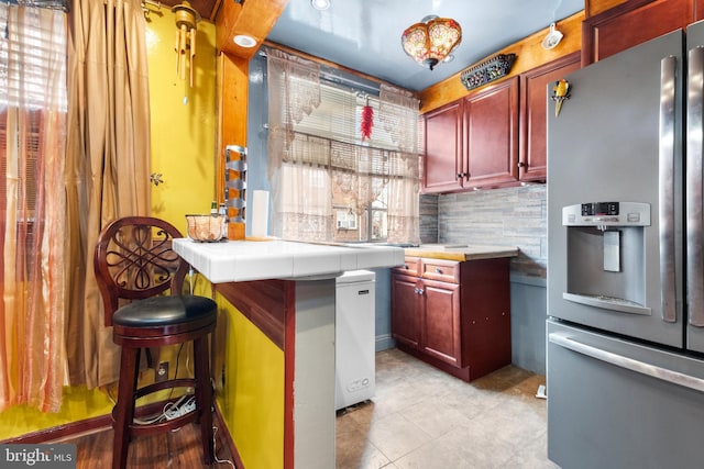 interior space featuring backsplash, stainless steel refrigerator with ice dispenser, and light tile patterned floors