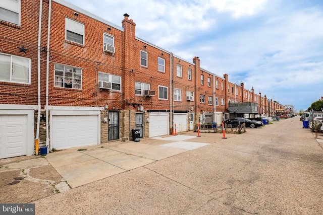 view of building exterior with an attached garage, driveway, a residential view, and cooling unit