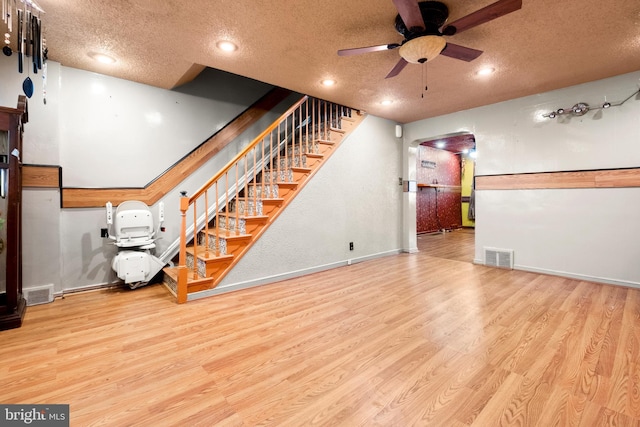 below grade area with wood finished floors, visible vents, a textured ceiling, and ceiling fan