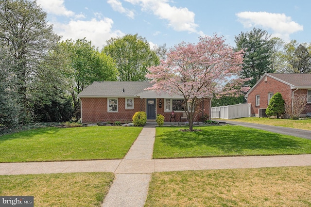 ranch-style home featuring brick siding, fence, a front yard, and central air condition unit