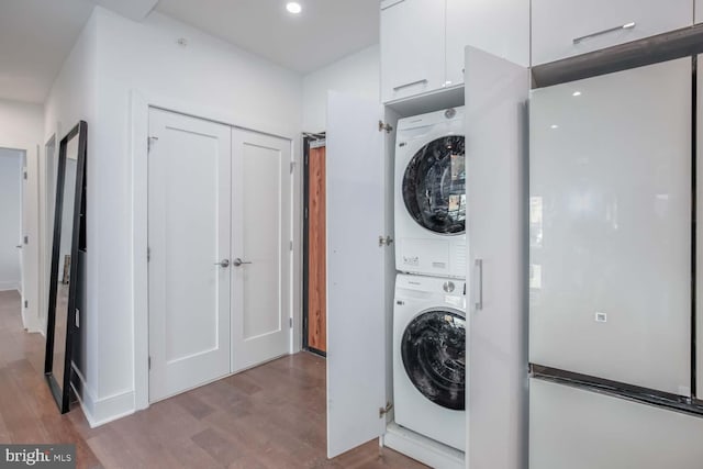 laundry room featuring recessed lighting, wood finished floors, stacked washer / dryer, and laundry area
