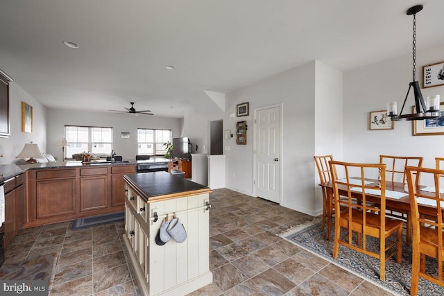 kitchen featuring brown cabinets, dark countertops, ceiling fan, a sink, and stone finish flooring