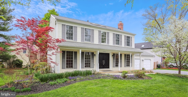 colonial house with a front lawn, driveway, a chimney, covered porch, and an attached garage