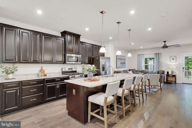 kitchen featuring stainless steel appliances, open floor plan, a kitchen island with sink, a breakfast bar, and light stone countertops