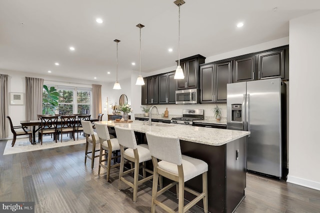 kitchen featuring stainless steel appliances, a sink, a center island with sink, light stone countertops, and a breakfast bar area
