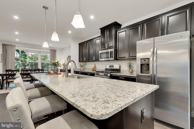 kitchen featuring stainless steel appliances, a sink, an island with sink, a breakfast bar area, and light stone countertops