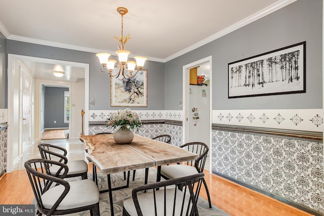 dining area with light wood-style flooring, crown molding, a chandelier, a wainscoted wall, and baseboards