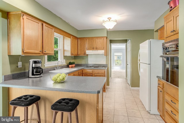 kitchen with a sink, white appliances, a peninsula, under cabinet range hood, and a breakfast bar area