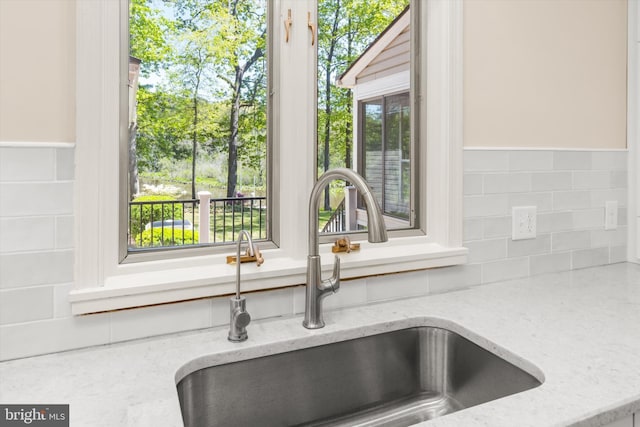 interior details featuring a sink, tasteful backsplash, and light stone countertops