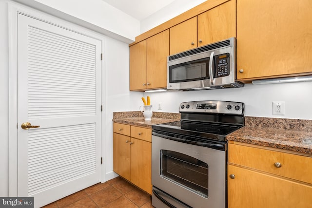 kitchen with tile patterned flooring, dark stone counters, and stainless steel appliances
