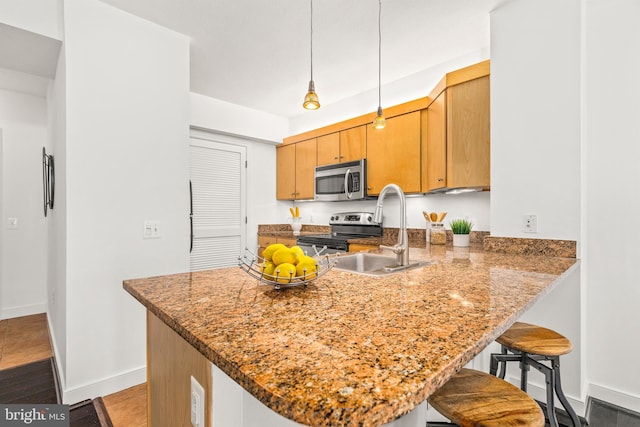 kitchen with a breakfast bar area, a sink, baseboards, a peninsula, and stainless steel appliances
