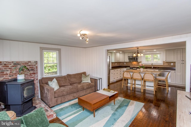 living area with dark wood-style flooring, a notable chandelier, a healthy amount of sunlight, and a wood stove