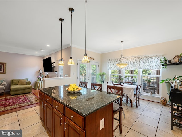 kitchen featuring light tile patterned floors, a center island, a breakfast bar, ornamental molding, and open floor plan
