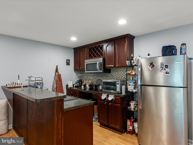 kitchen featuring decorative backsplash, light wood-style floors, a toaster, dark countertops, and appliances with stainless steel finishes