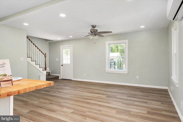 unfurnished living room with plenty of natural light, a wall unit AC, ceiling fan, light wood-type flooring, and recessed lighting