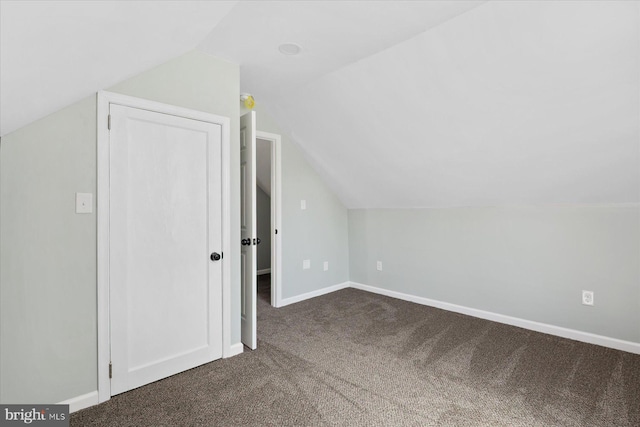 additional living space featuring dark colored carpet, lofted ceiling, and baseboards