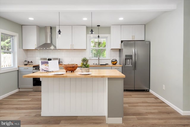 kitchen featuring stainless steel appliances, wall chimney exhaust hood, wooden counters, a center island, and backsplash