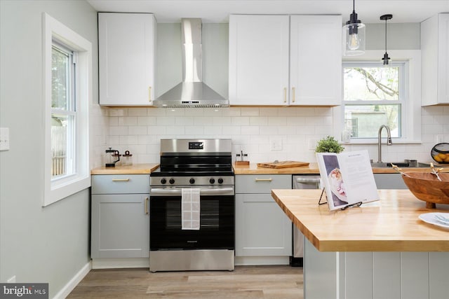 kitchen featuring wooden counters, electric stove, wall chimney range hood, light wood-style floors, and hanging light fixtures