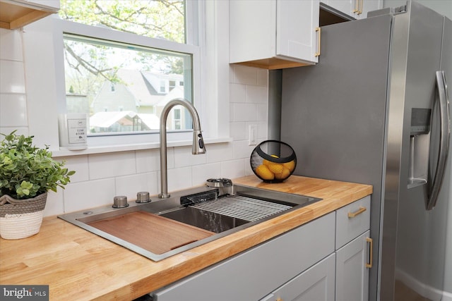 kitchen with stainless steel refrigerator with ice dispenser, a sink, backsplash, and wooden counters