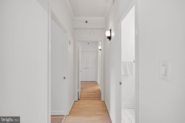 hallway with light wood-type flooring, ornamental molding, and baseboards