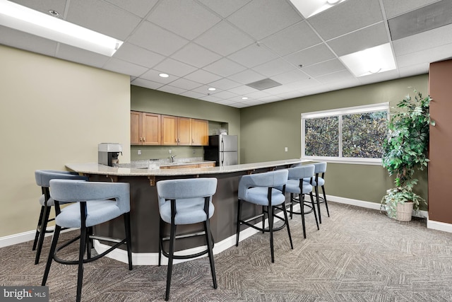 kitchen featuring light colored carpet, a kitchen breakfast bar, freestanding refrigerator, a peninsula, and baseboards