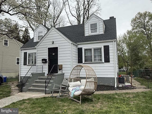 new england style home featuring a front lawn, a shingled roof, and fence