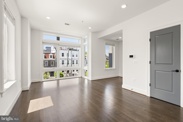 unfurnished living room featuring plenty of natural light, baseboards, dark wood-style floors, and visible vents