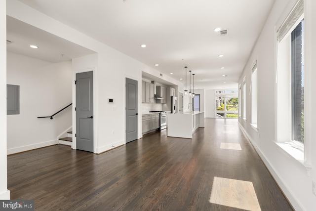 unfurnished living room with dark wood finished floors, stairs, recessed lighting, baseboards, and electric panel
