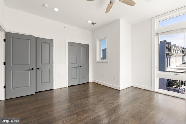 unfurnished bedroom featuring recessed lighting, baseboards, two closets, and dark wood-style flooring