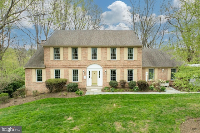 colonial-style house featuring brick siding, roof with shingles, and a front yard