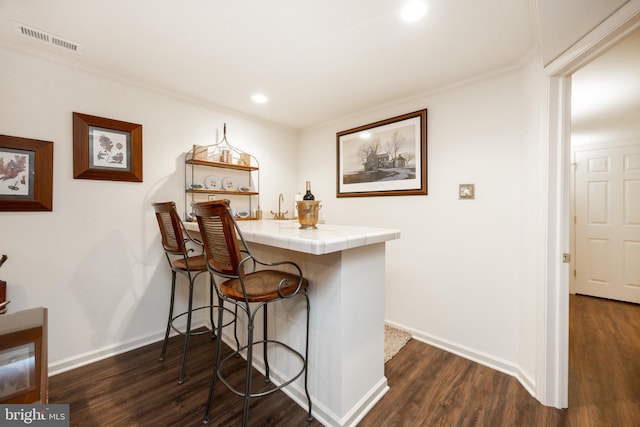 kitchen with a peninsula, visible vents, a kitchen bar, tile counters, and dark wood-type flooring