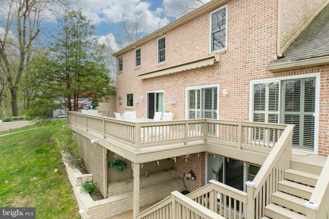 rear view of property with a lawn, brick siding, stairs, and a deck