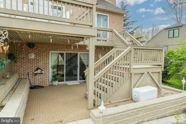 exterior space featuring a wooden deck, brick siding, stairs, and a patio