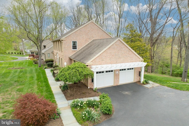 view of side of home featuring roof with shingles, driveway, brick siding, a garage, and a lawn