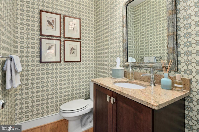 half bath with wallpapered walls, vanity, and toilet