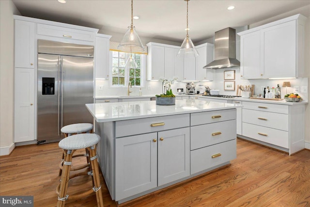 kitchen with wall chimney range hood, a center island, light wood-type flooring, stainless steel appliances, and white cabinets