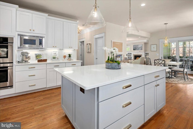 kitchen with light countertops, light wood-style flooring, decorative light fixtures, and stainless steel appliances