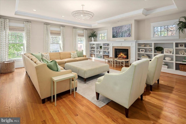 living room featuring a tray ceiling, plenty of natural light, and light wood-style flooring